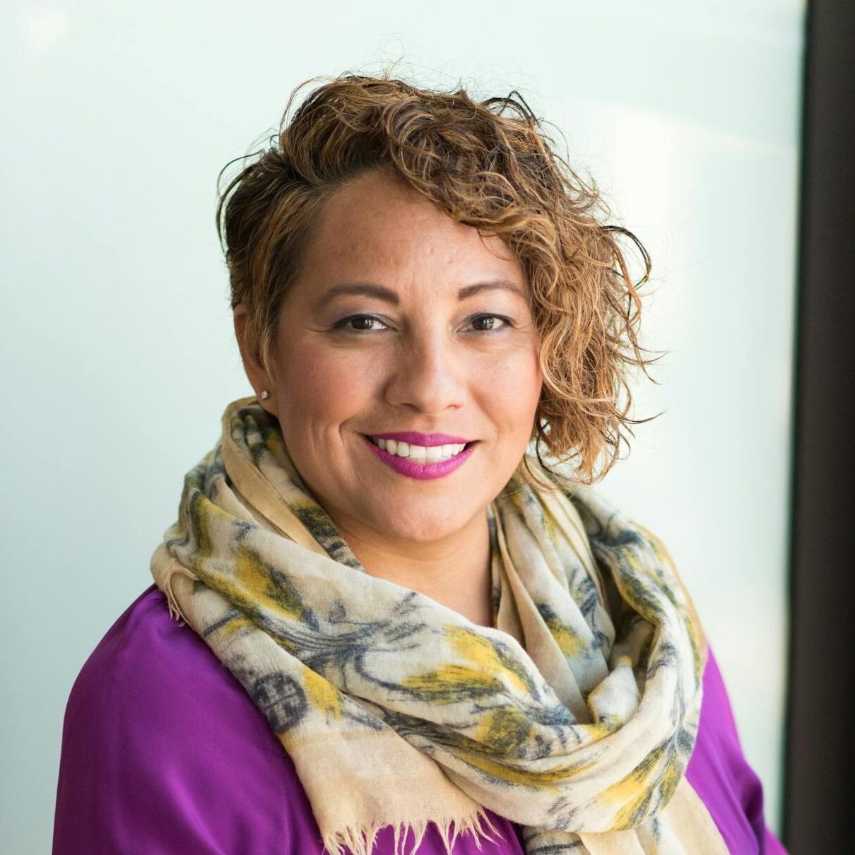 Smiling woman in a purple dress and scarf holding a tablet indoors.