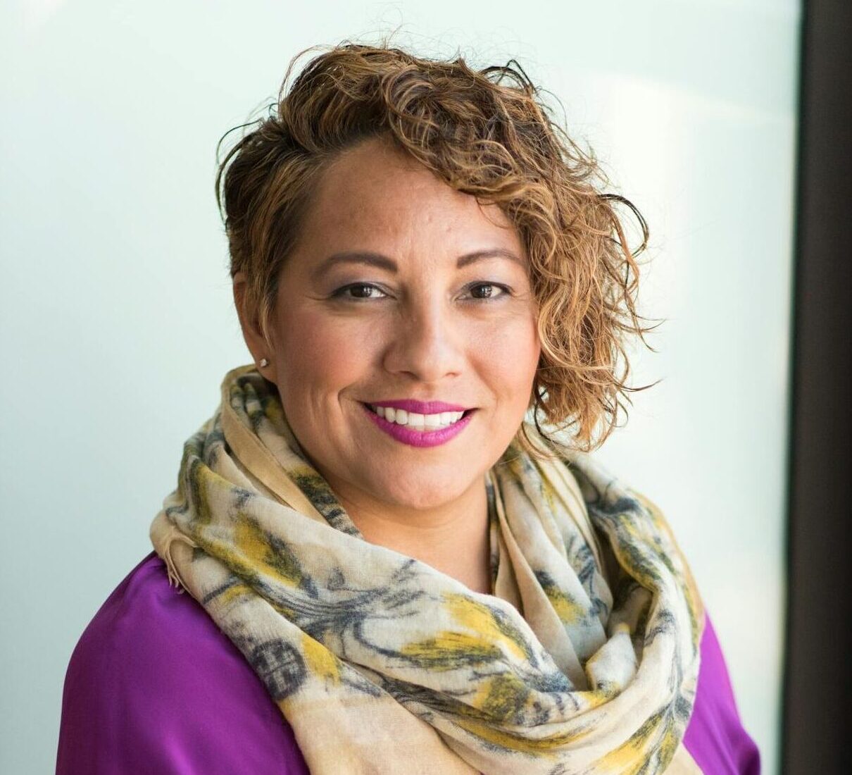 Smiling woman in a purple dress and scarf holding a tablet indoors.